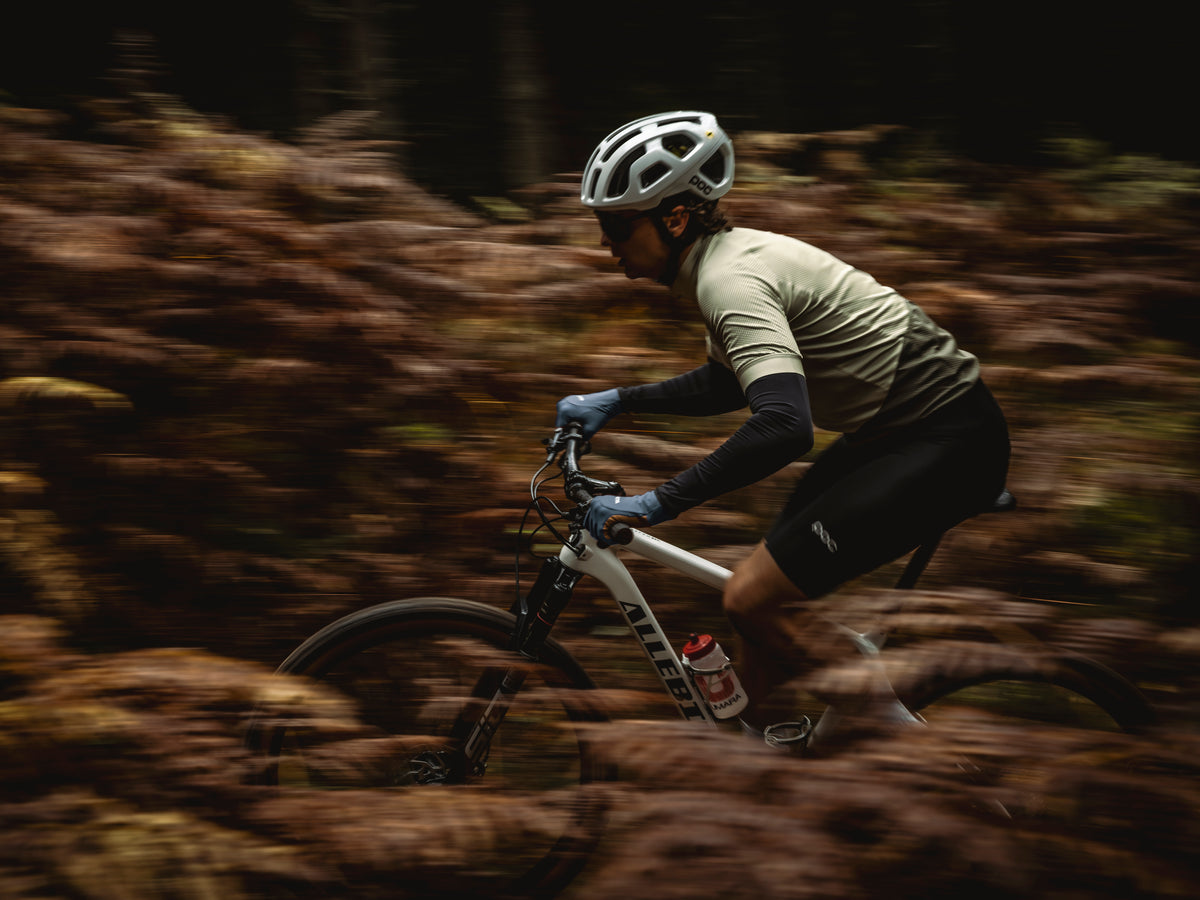 Biker wearing blue gloves rides a forest trail, with motion blur highlighting speed through autumn terrain.
